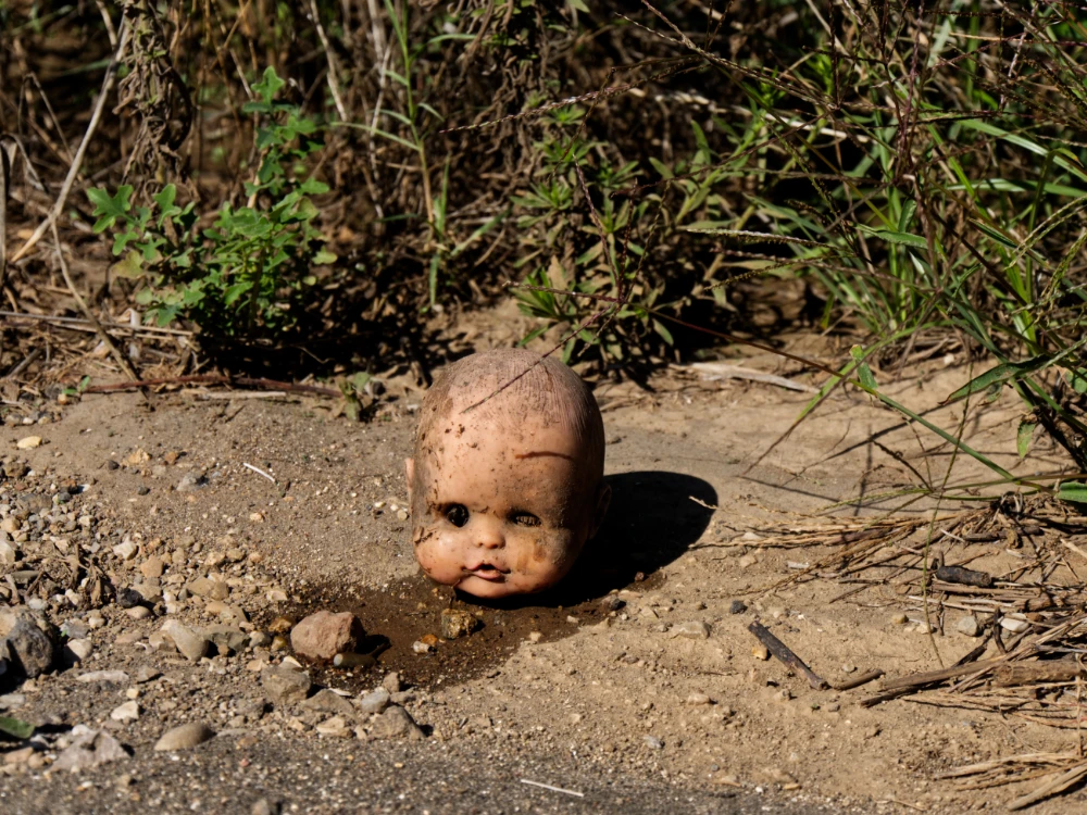 A discarded doll’s head half-buried in dry ground