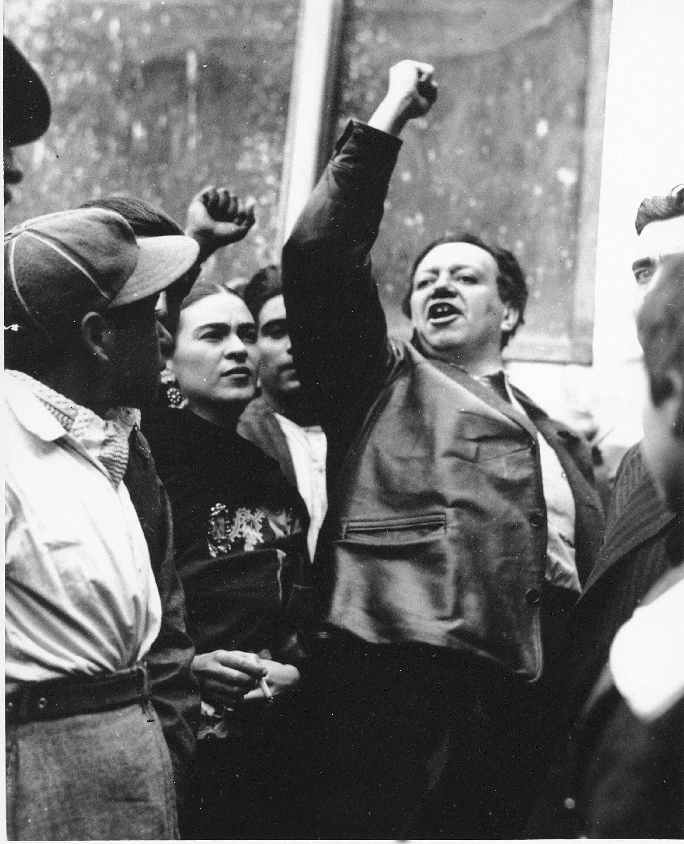 Black-and-white photograph of Frida Kahlo beside a man raising his fist in a crowd